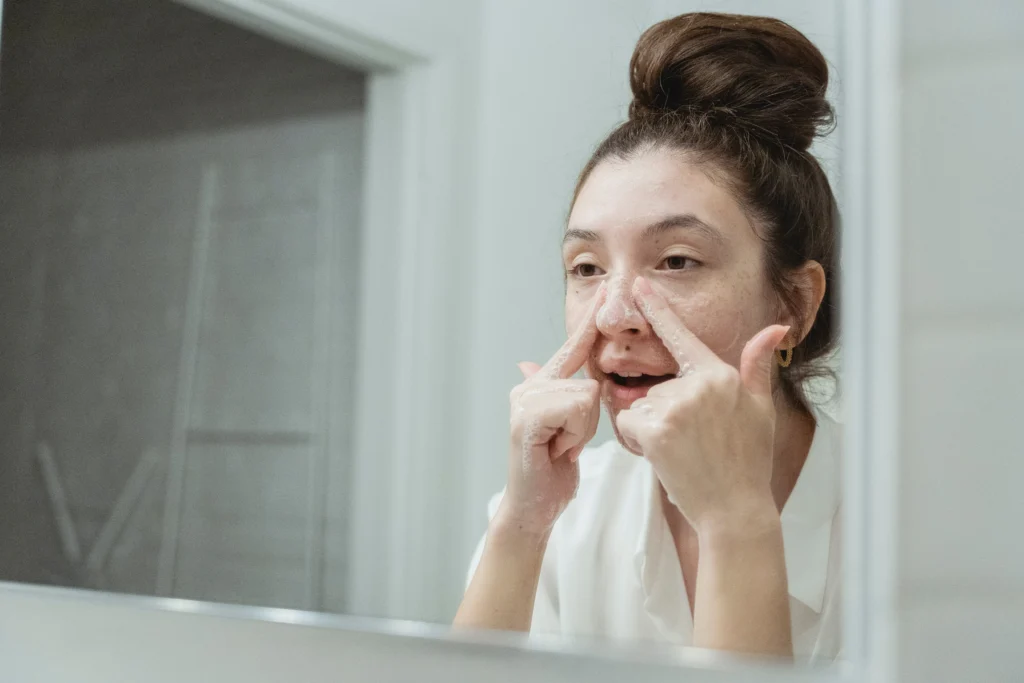Mujer utilizando un limpiador facial antiacné frente al espejo.