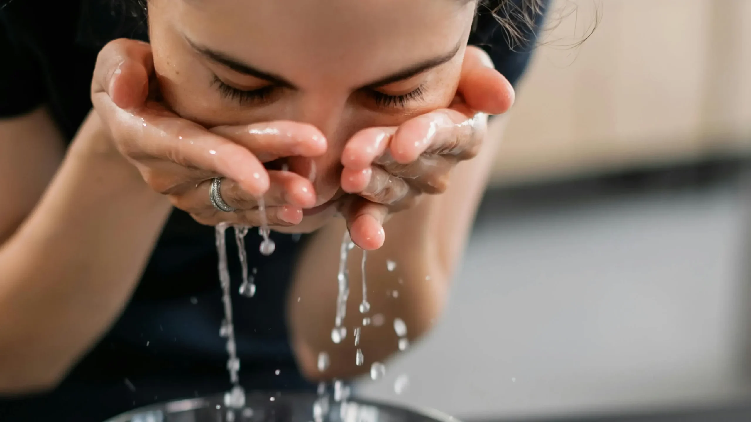 Mujer lavando su cara con pie grasa, acneica y deshidratada con agua.